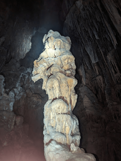 A tall, illuminated stalagmite in a dark cave, showcasing intricate rock formations and textures.